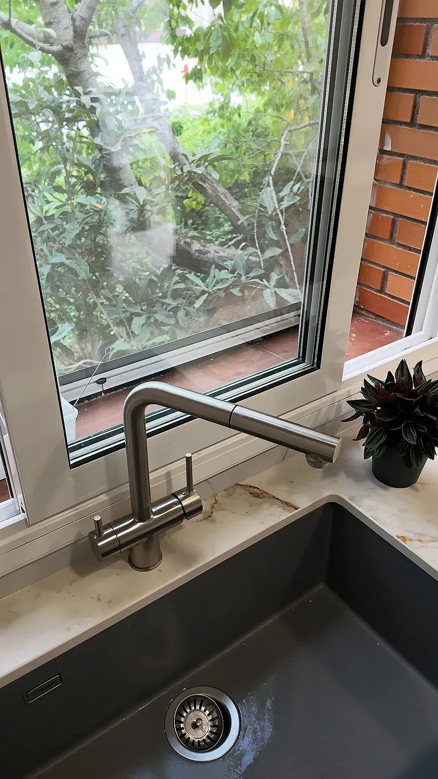 Fregadero de granito gris y grifo extraíble de acero bajo la ventana, cocina de Terrassa
