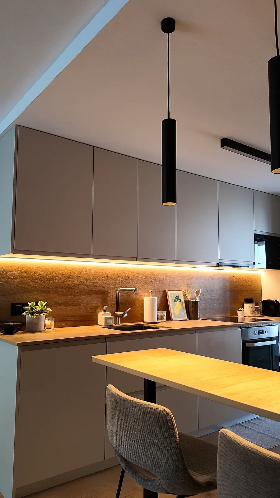 Cocina abierta con barra de madera, frentes en tono topo y lámparas colgantes negras, Castelldefels