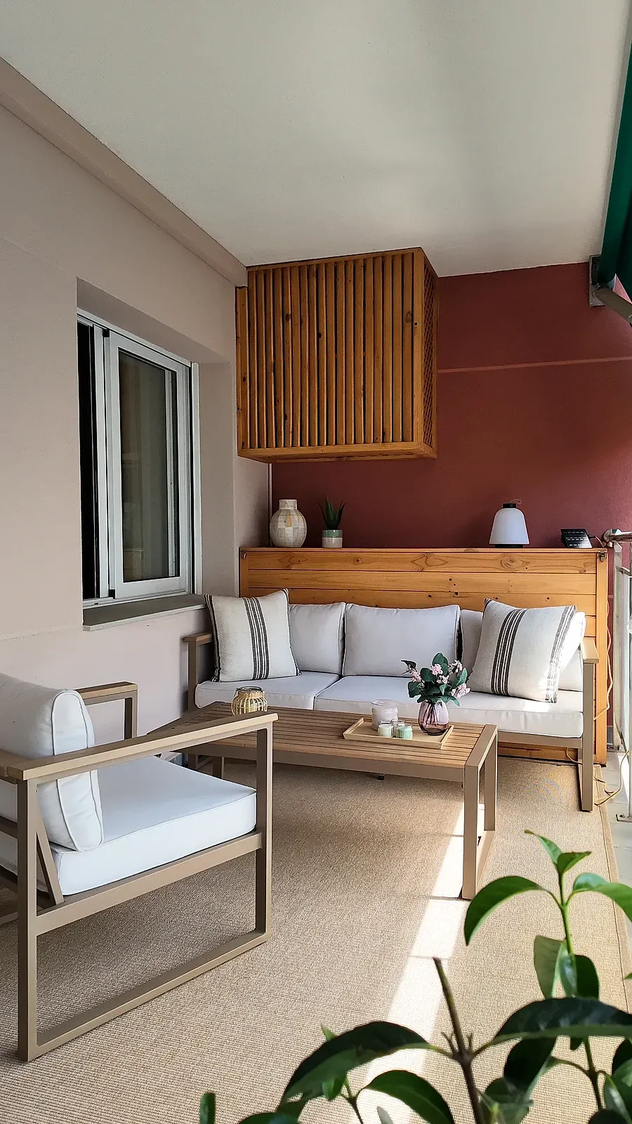 Terraza con sofá de madera, cojines blancos y pared en tono teja, reforma de Castelldefels