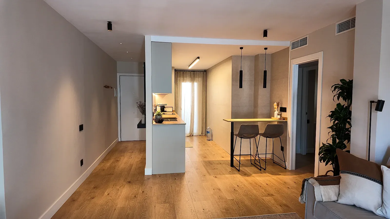 Salón comedor abierto a la cocina en Castelldefels, con suelo de madera y barra al fondo