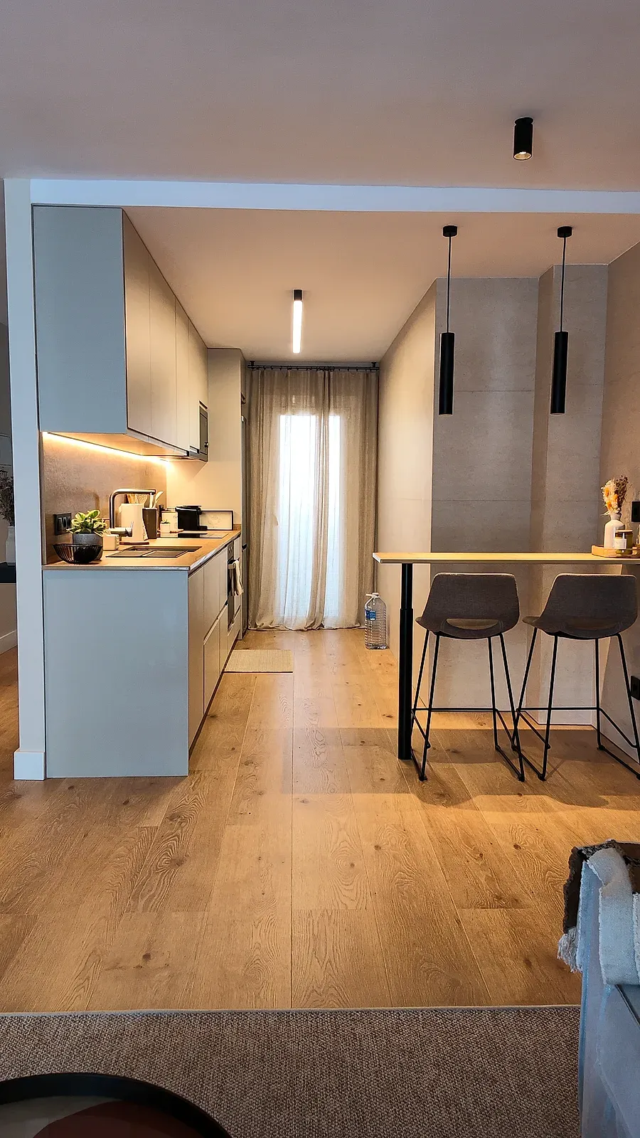 Espacio abierto de cocina y comedor con barra de madera, taburetes y lámparas colgantes, Castelldefels